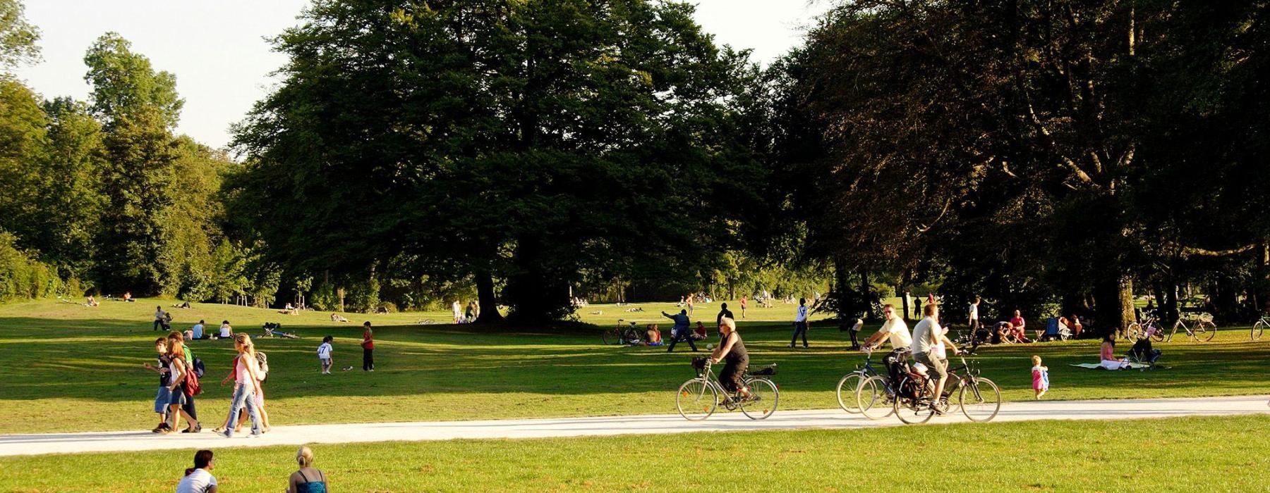 A park with many people riding bikes, having a picnic, and walking.